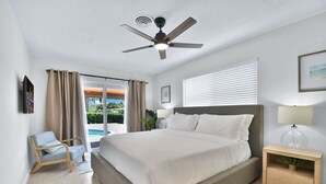 A hotel room with a large bed, a ceiling fan, a bedside table with a lamp, a chair, and a view of a swimming pool. - 6341 Managed By Brampton Park (Fort Lauderdale)