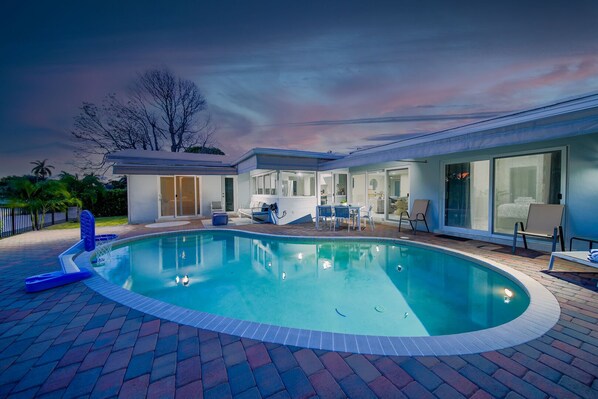 Une maison moderne dotée d’une piscine, de mobilier de jardin et d’un espace extérieur couvert.