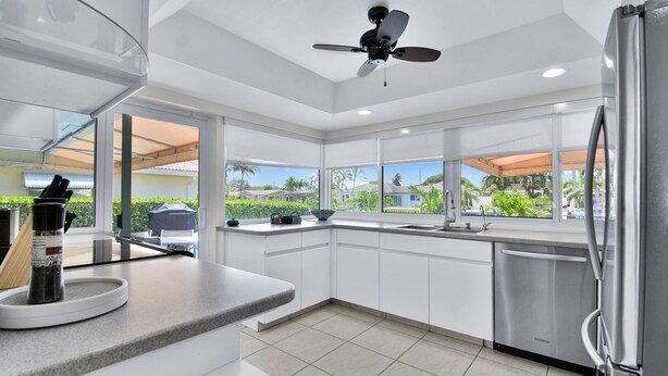 A modern kitchen with white cabinetry, a stainless steel refrigerator, and a window overlooking a residential area. - 6341 Managed By Brampton Park (Fort Lauderdale)