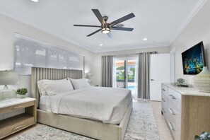 Une chambre à coucher moderne, équipée d’un lit, de tables de chevet, d’un ventilateur de plafond et offrant une vue sur l’extérieur.