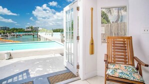 A room with a view of a swimming pool, a wooden chair with a floral cushion, and a wooden paddle leaning against the wall.