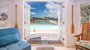 A room with a view of a pool, a blue sofa, a wooden chair, and two wooden bathtubs.