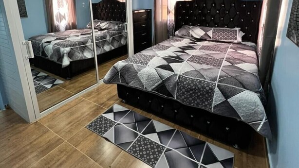 A bedroom with a mirrored closet, a bed with a geometric-patterned bedspread, and a wooden floor.