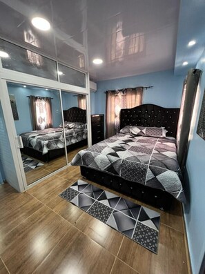 Un dormitorio con armario espejado, cama con colcha de estampado geométrico y suelo de madera.
