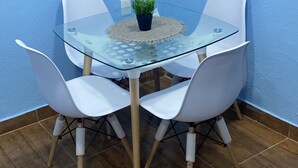 A glass-top table with four white chairs, a small potted plant, and a white electrical outlet on a blue wall.