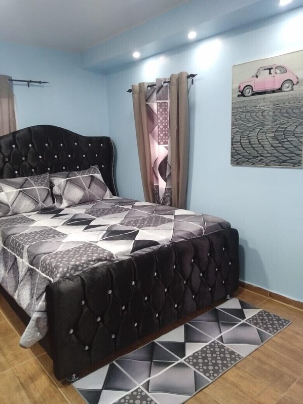 Un dormitorio con cabecera acolchada, colcha estampada y alfombra de diseño geométrico.