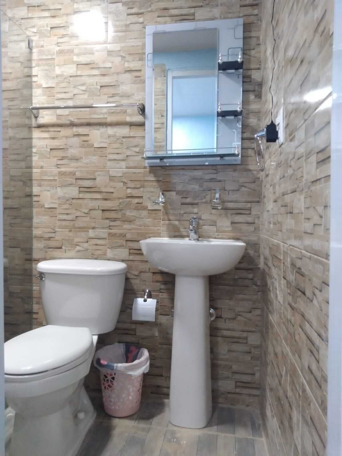 A bathroom with a stone-patterned wall, a white sink, and two toilets.