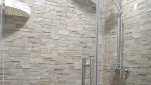A glass-enclosed shower with a stone-patterned wall, a handheld showerhead, and a handheld shower hose.