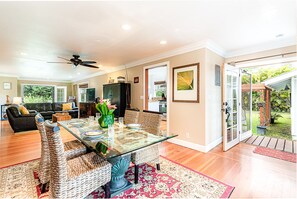 Relax in this inviting living area with a glass-top dining table and wicker chairs, surrounded by a large window offering a view of the outdoors.