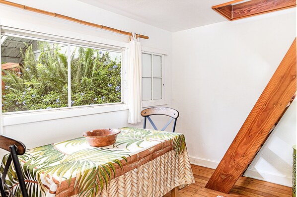A room with a table set for dining, a window with a view of greenery, and a wooden structure leaning against the wall.