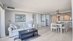 Uma sala de estar moderna com sofá, mesa de centro e área de jantar com cadeiras e um candelabro.