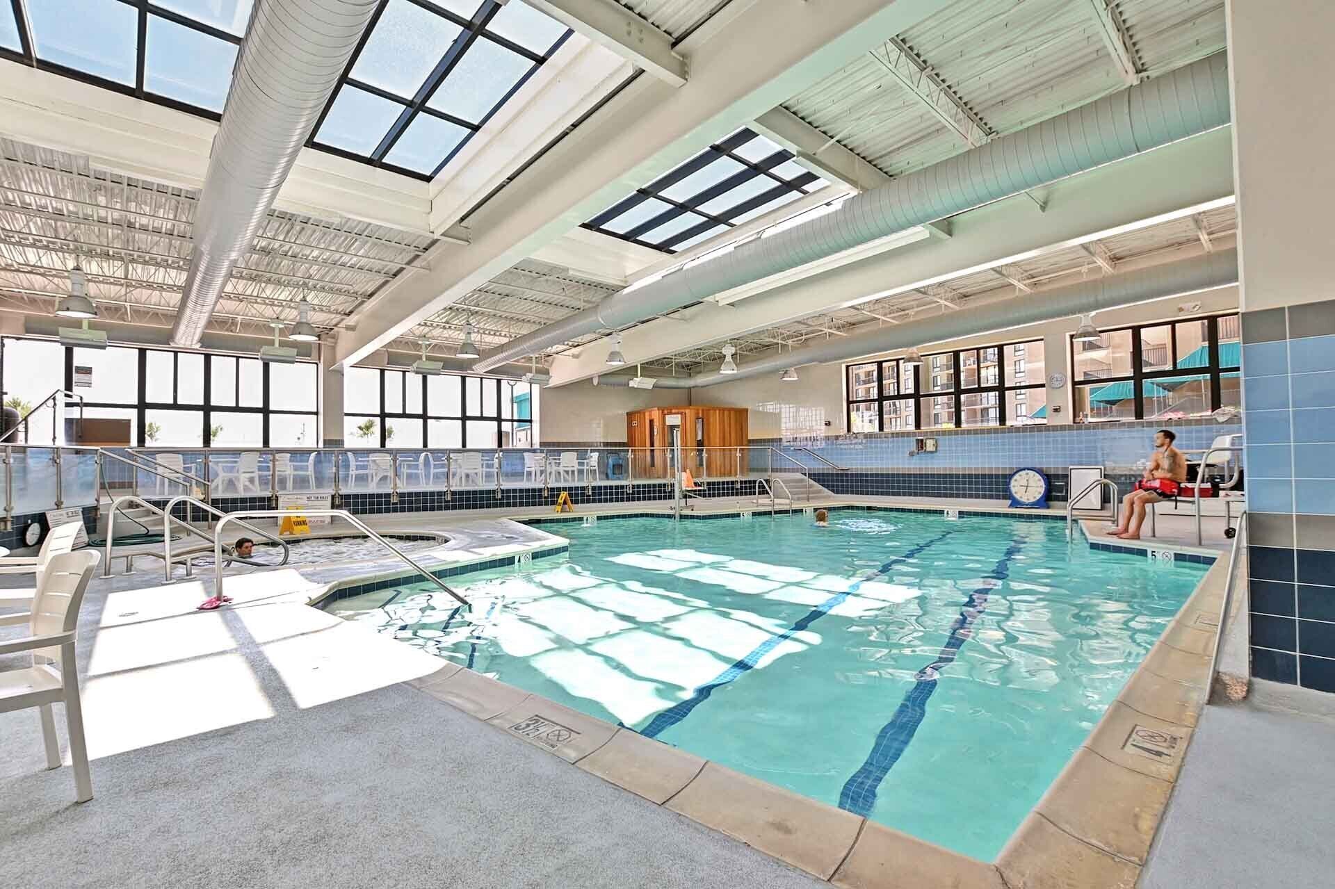 An indoor swimming pool with clear water, a diving board, and a lifeguard chair.