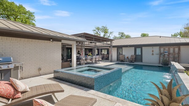 A backyard with a swimming pool, outdoor seating, and a barbecue grill.