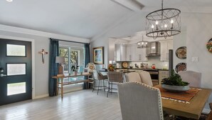 A modern kitchen with white cabinets, a dining area with a wooden table and chairs, and a chandelier.