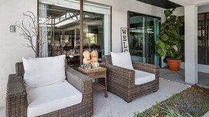 A wicker outdoor seating area with two chairs and a small table, a large potted plant, and a 'WELCOME' sign.