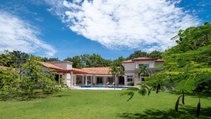 A two-story house with a swimming pool, surrounded by a well-maintained lawn and trees.