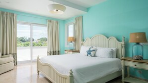 A bedroom with a bed, two nightstands, a lamp, a chair, and a view of greenery outside.
