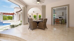 A spacious indoor area with a dining table and chairs, a ceiling fan, and a view of a swimming pool outside.