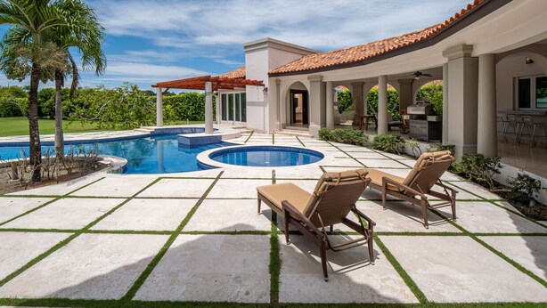 A pool area with two lounge chairs, a pergola, and a covered patio with a dining area.