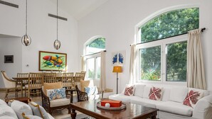 A spacious living room with a white sofa, wooden coffee table, and a dining area with wooden chairs and a table.