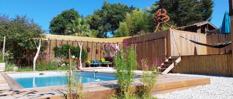 A backyard with a wooden deck, a pool, and a hammock.