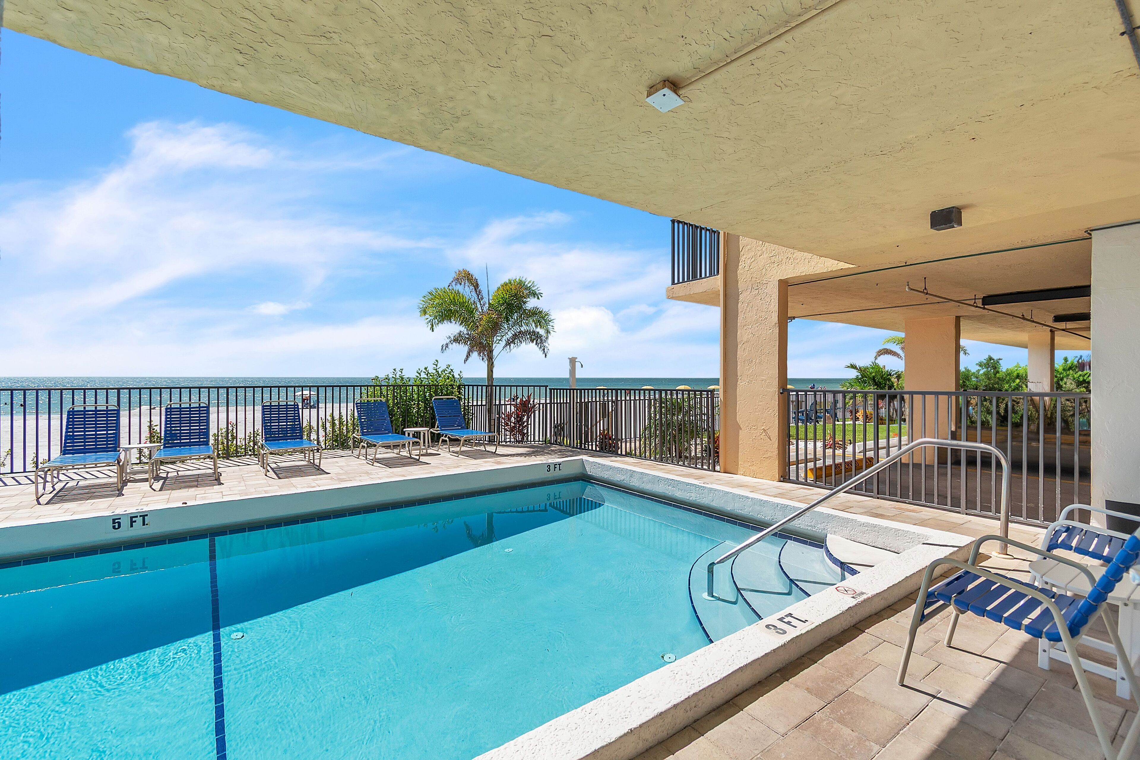 A swimming pool with a view of the ocean, surrounded by lounge chairs and a railing.