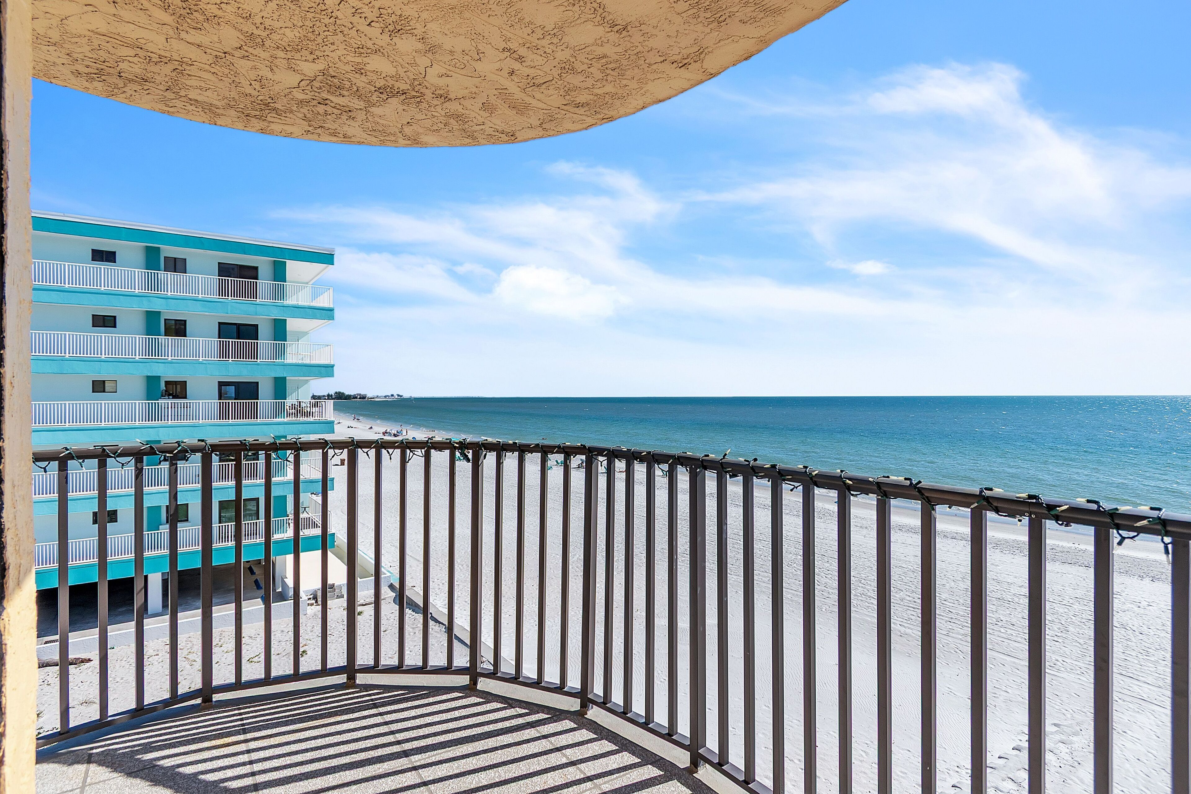 Ein Balkon mit Blick auf einen Strand und ein Gebäude mit mehreren Balkonen.