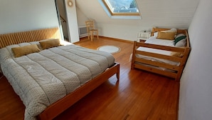 Une chambre à coucher avec un lit en bois, une petite chaise en bois, une table de chevet et une lucarne.