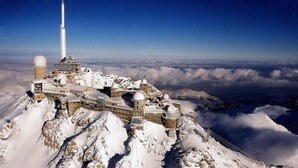 Un observatoire de montagne enneigé, doté d’une haute tour, de bâtiments à coupole et surplombant un ciel dégagé.