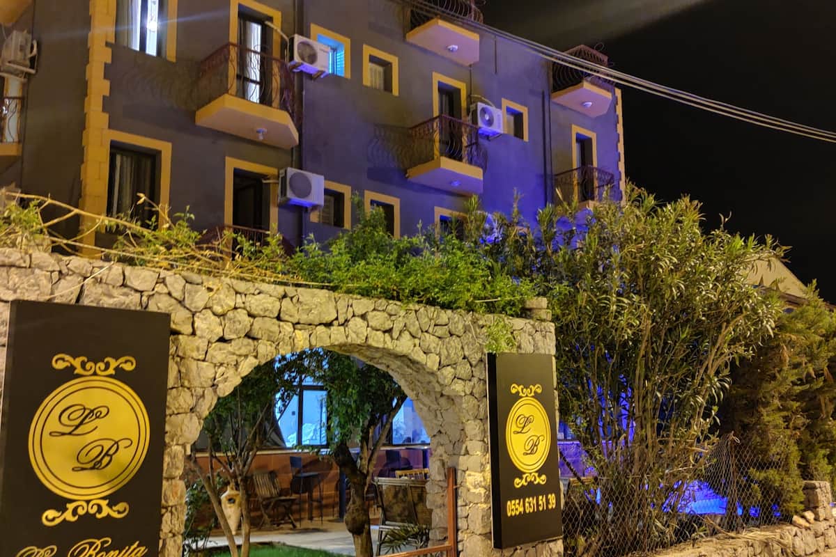 A stone archway leading to a building with balconies and air conditioning units. There are two signs with a logo and contact number.