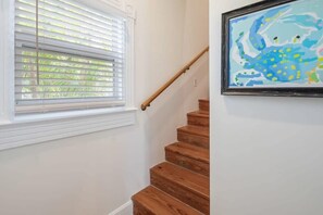 Eine Treppe mit Holzboden und einem Holzgeländer, die zu einem Raum mit weißen Wänden und einem Fenster mit Jalousien führt.