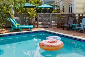 Une piscine entourée d’une terrasse en bois et d’une clôture, avec des chaises longues et des parasols à proximité.