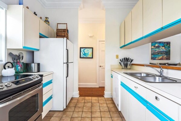 A compact kitchen with white cabinets, blue accents, a stainless steel sink, and a built-in oven.