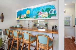 Eine Küche mit Barbereich, Korbstühlen und einem farbenfrohen Bild über der Arbeitsfläche.