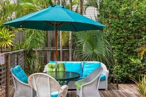 A patio with wicker furniture, a round table, and a teal umbrella.