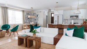 Un salon moderne avec un canapé blanc, des fauteuils verts et une cuisine en arrière-plan.