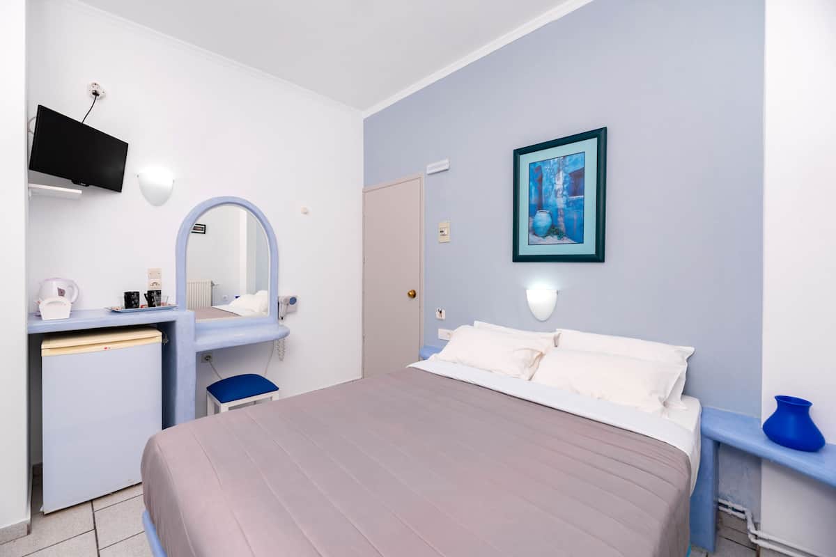 A hotel room with a bed, a desk with a mirror, a television, and a painting on the wall.