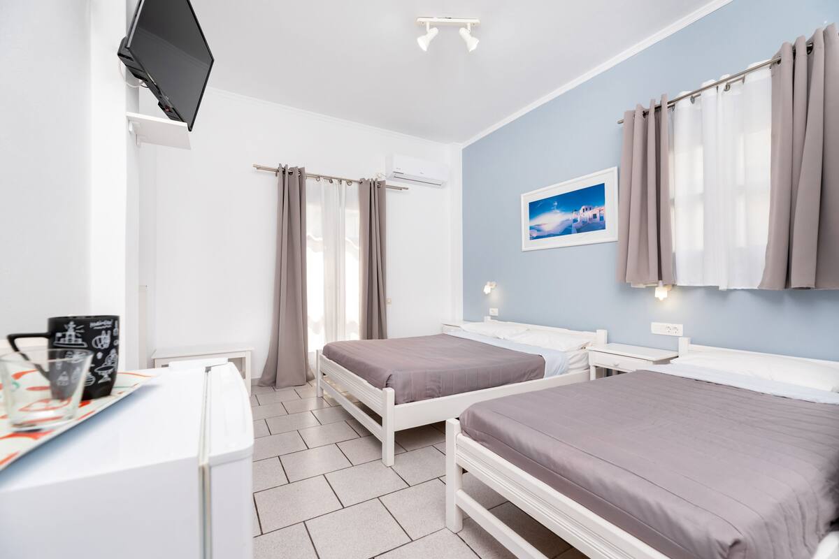 A hotel room with two beds, a desk, a flat-screen TV, and a window with curtains.