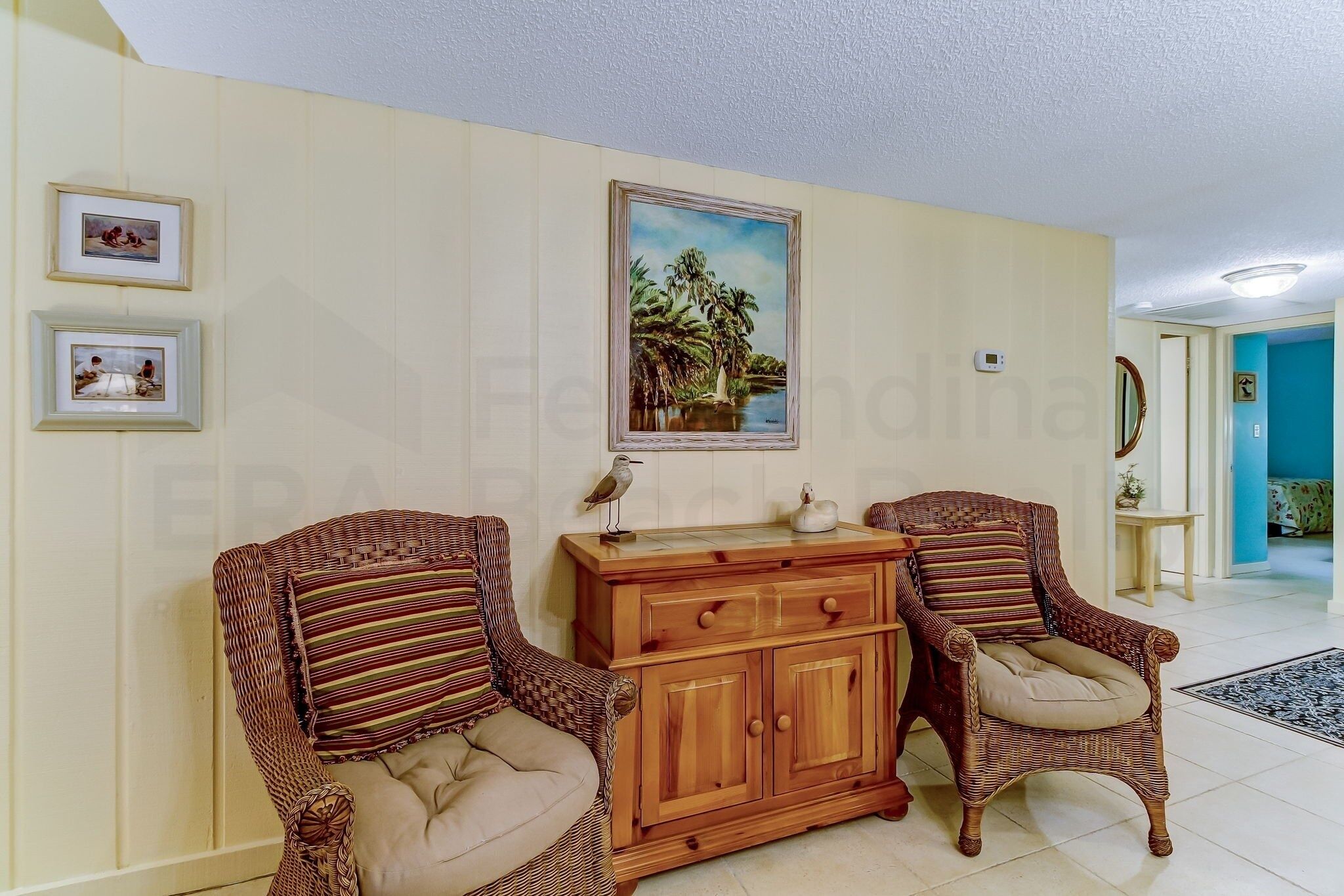 A room with two wicker chairs, a wooden cabinet, and framed pictures on the wall.