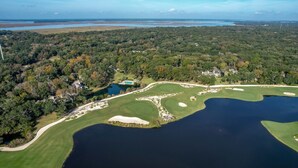 An aerial view of a golf course with multiple bunkers, a pond, and surrounding forested areas. - Dog Friendly Beach Wood Condo, Minutes Away from Atlantic Ocean by RedAwning (Fernandina Beach)
