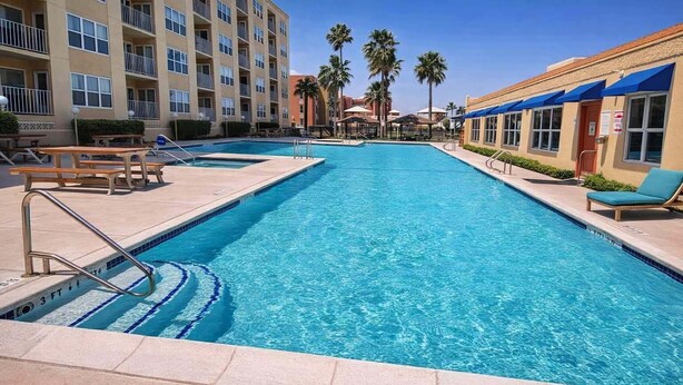 A swimming pool with a 3 FT depth marker, lounge chairs, and a building with multiple balconies.