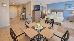 A hotel room with a bed, a TV, a dining table with chairs, and a kitchenette.