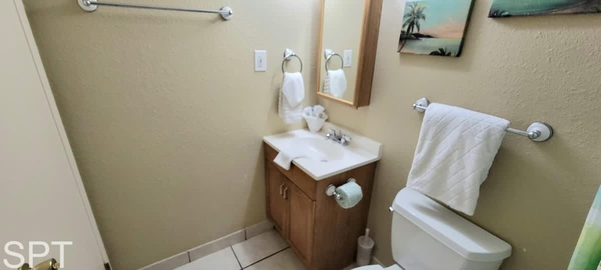 Un baño con tocador de madera, lavamanos blanco, inodoro y perchero para toallas.