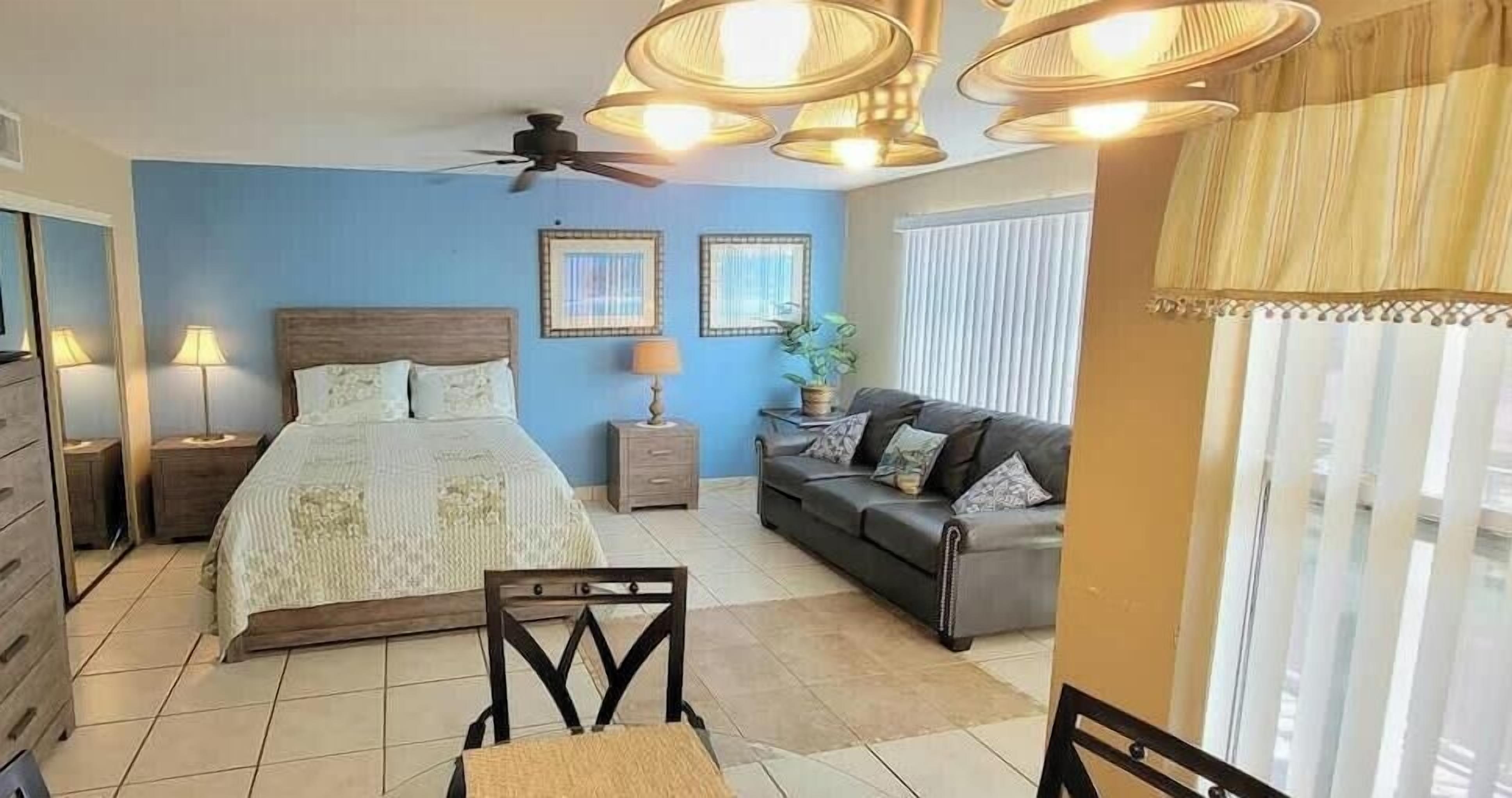 A bedroom with a bed, bedside tables, a TV, a ceiling fan, and a window with curtains.