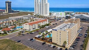 A coastal hotel area with multiple buildings, including a prominent hotel with a pool and a parking lot.