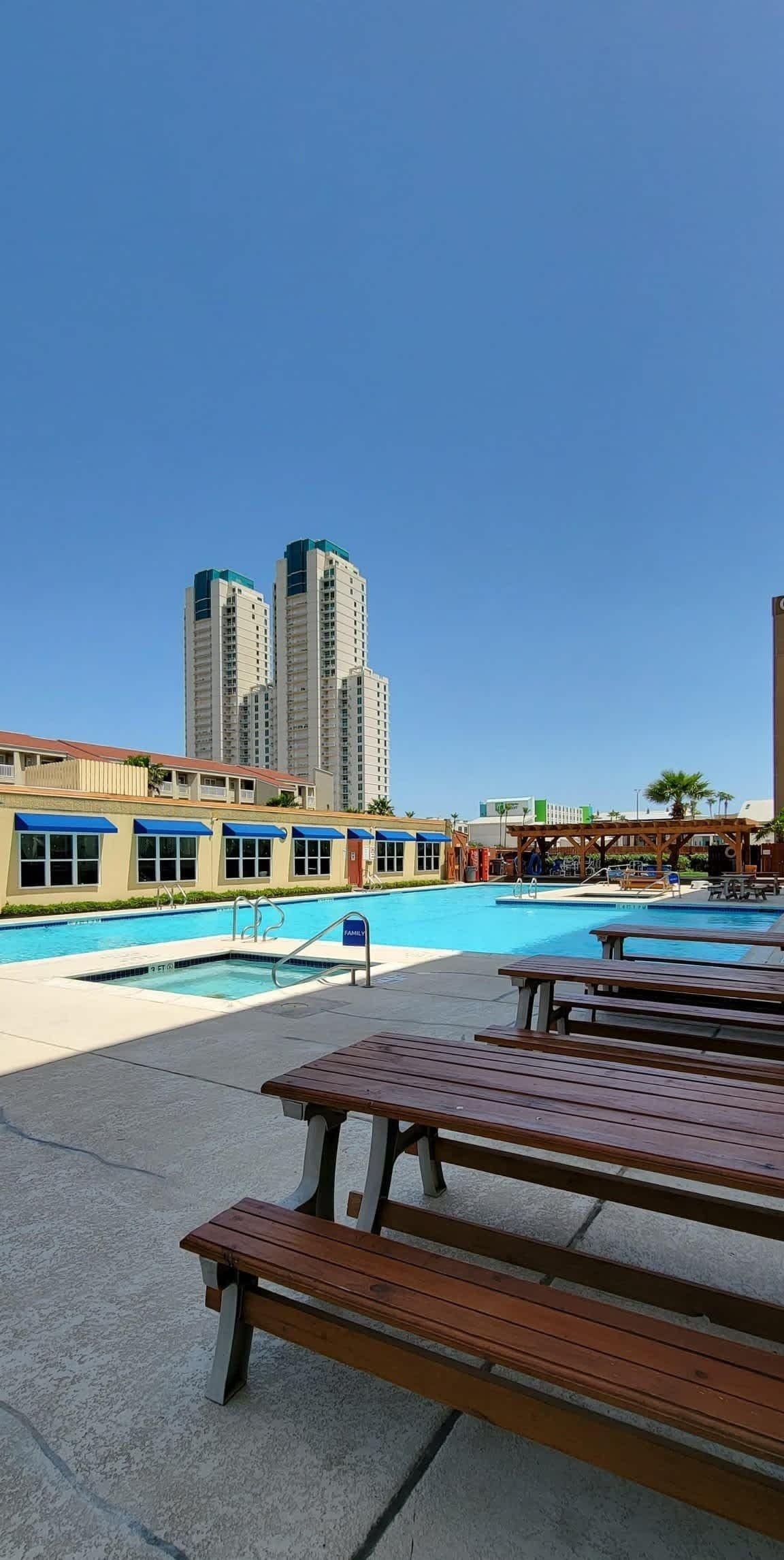A pool area with picnic tables and a building with a blue awning in the background.
