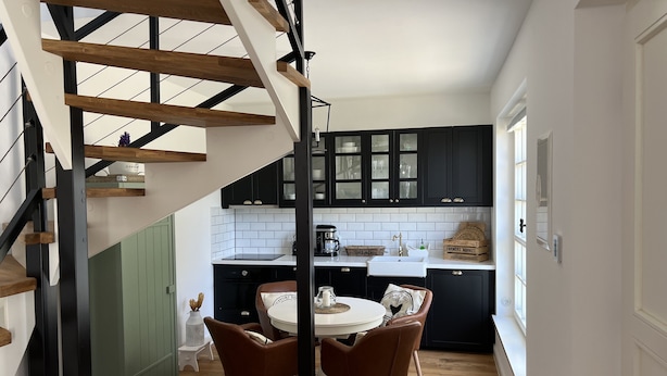Una cocina moderna con escalera de madera, armarios negros y un comedor con mesa y sillas redondas.