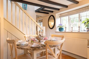 A dining area with a wooden table set for four, surrounded by chairs. A staircase with wooden railings is visible to the left.