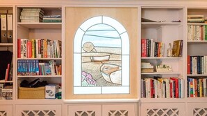 A room with a bookshelf filled with books, a decorative stained glass window, and a woven basket.