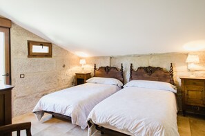 Un dormitorio con dos camas individuales, cabeceros de madera, paredes de piedra y lámparas de noche.